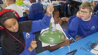 Three children wearing headphones tap a green lampshade.