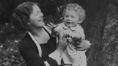 Black and white photograph of a woman holding an infant in a garden. Both have big smiles.