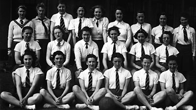 A school photo-style picture of a netball team - 21 women in three rows. All wear white shirts with ties. 