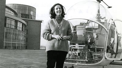 Yvonne Littlewood stands cheerfully on the roof of 鶹Լ Television Centre next to a 1960s helicopter with a round glass cockpit.