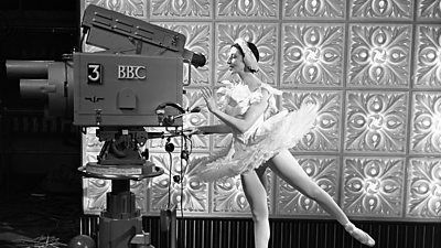 Ballerina Alicia Markova pirouetting while she poses as if operating a large 鶹Լ studio camera.