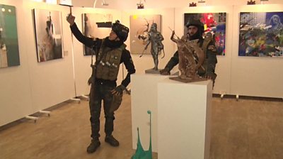 Two Iraqi soldiers, including one taking a selfie next to a sculpture