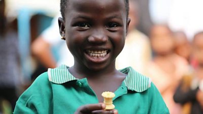 Young Nigerian girl holds chess piece and smiles wearing green shirt