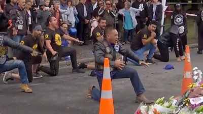 Bikers performing a haka dance next to flowers