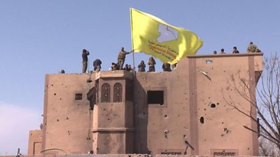 Kurdish-led fighters in eastern Syria raise a yellow flag as they celebrate the defeat of IS