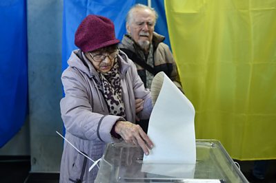 A voter attempts to post her comically long ballot paper in the ballot box