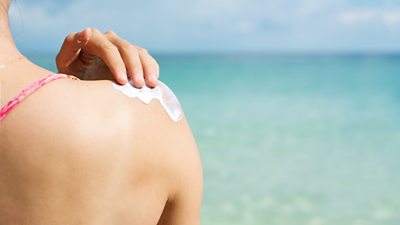 A woman rubs sun cream onto her back
