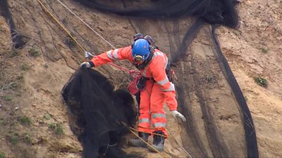 Workman removing nets from cliff