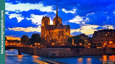 An evening shot of Notre-Dame cathedral in Paris. It is illuminated by orange lighting.