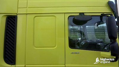 Yellow HGV cab with driver using mobile at wheel