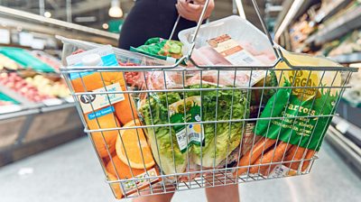 Closeup of a basket of shopping, held by a shopper, inside a Morrisons supermarket