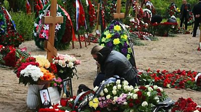 A woman kneels by the grave of one of the soldiers