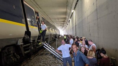Eurostar passengers mill around around outside the train in a tunnel