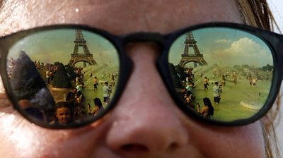 People cooling off in the Trocadero fountains across from the Eiffel Tower are reflected in sunglasses in Paris