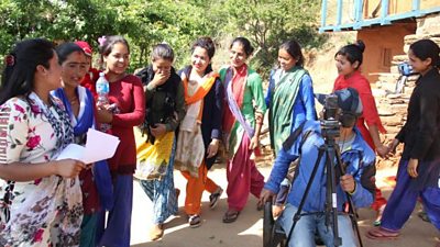 A group of 10 women gather to sing a song, some of them are taking it more seriously than others