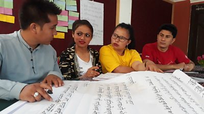 A man writes down ideas from three women on a large sheet of paper