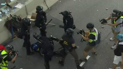 Police hold a protester pinned to the ground while news cameras record it