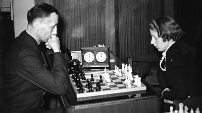 A man ponders his next chess move while his female opponent looks on