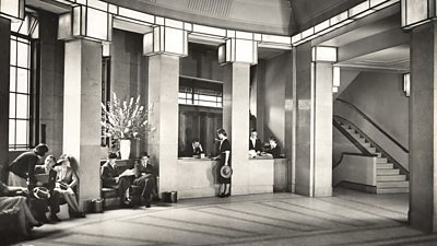 The entrance hall of Broadcasting House in 1939, men and women in smart clothes sit around the art deco opulence 