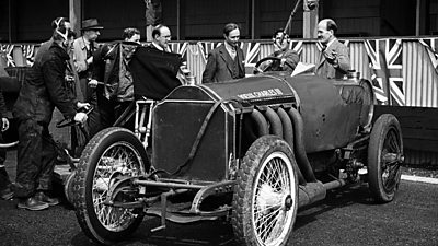 A racing driver and his pre-war racing car with large radiator is filmed by a TV camera