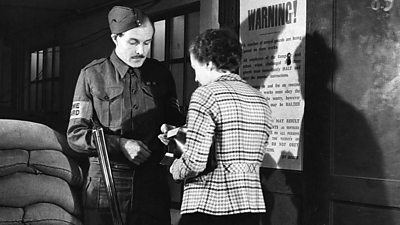 A ˿ Guard soldier with an uncocked shotgun inspects a woman's pass. There are sandbags to their left.