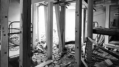 Bomb damage inside a sleeping quarter at ˿ Maida Vale. There is a hole in the roof and a large amount of rubble.