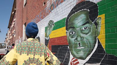 A man stands next to a mural of Robert Mugabe