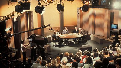 The Question Time studio in 1979 with the audience looking on as the panelists sit around an oval table. 