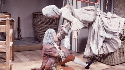 Terry Jones as Joseph Montgolfier and Carol Cleveland as his fiancee, Antoinette, who is dangling from a strap on the ceiling. Both are in 18th century French aristocrat costumes.