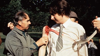 Eric Idle has a prosthetic severed arm attached by a member of the props department