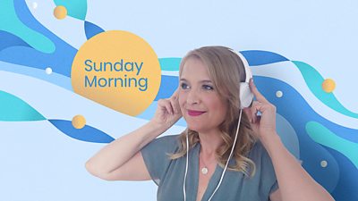 Radio 3 Sunday Morning presenter Sarah Walker has what headphones on and stands in front of a Sunday Morning sign.