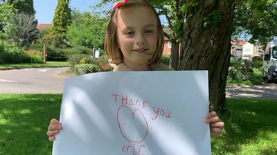 Nella who was helped by the charity Eric,the Children's Bowel and Bladder Charity holding a white sign where she has drawn a smiley face and written the words thank you Eric