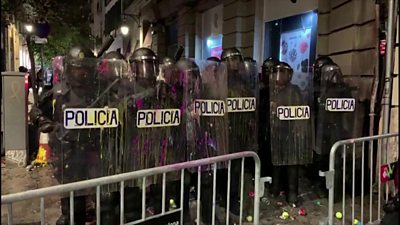 Riot police stand in formation after being pelted with paint