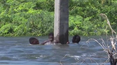 People cling to an electricity post with flood water up to head height