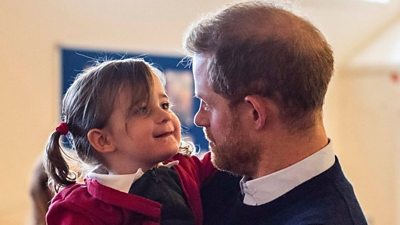 Prince Harry picks up a little girl at Windsor's Broom Farm Community Centre