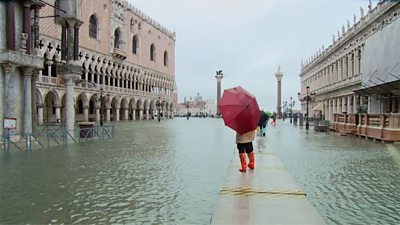 Woman stands with umbrella in flooded Venice