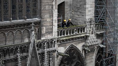 A close-up shot of the front of Notre Dame with scaffolding, and workmen on a balcony