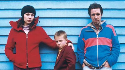 A mother and a father with their son stand in winter dress by a beach hut