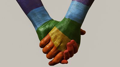 Men holding hands painted with rainbow colours