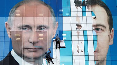 A poster of Vladimir Putin and Dmitry Medvedev being attached to an office building in 2011