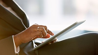 Women hand taps on digital tablet as she sits. Cropped so can't see her face