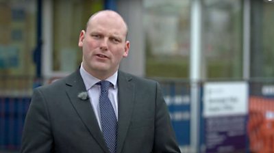 Panorama report Sean Dilley doing a piece to camera outside a police station which is soft focus in the background