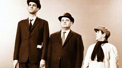 L-R: John Cleese, Ronnie Barker and Ronnie Corbett. A still of the 'class sketch' with Ronnie Corbett looking up to Barker and Cleese who are looking forward.