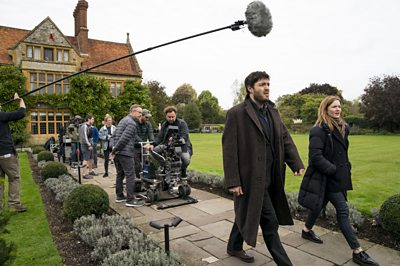 Cormoran Strike (TOM BURKE), Robin Ellacott (HOLLIDAY GRAINGER) **BEHIND-THE-SCENES**(Image Credit: BBC/Bronte Films/Steffan Hill)