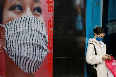 Woman in mask stands next to poster of woman wearing mask