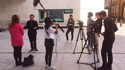 Six University Westminster students interviewing presenter Ros Atkins on the tv News Broadcasting House piazza in London, wearing masks.