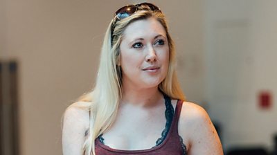 Melissa John looking away from the camera looking thoughtful. Long blonde hair with sunglasses on her head. Background is cream colours out of focus,