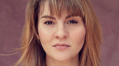 Headshot of Ruth Madeley. Looking straight into the camera. Background in out of focus and pink