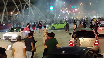 A screengrab from footage shows a stunt driver blocking an overpass in Atlanta, while pedestrians watch