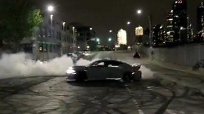 A driver spins doughnuts on a street in front of spectators, after dark